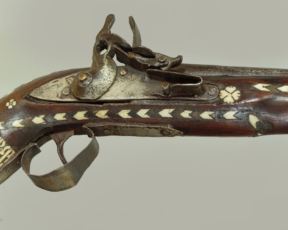 An antique Afghan Jezail musket featuring a distinctly curved wooden stock decorated with geometric bone inlay and a steel lock mechanism. View III