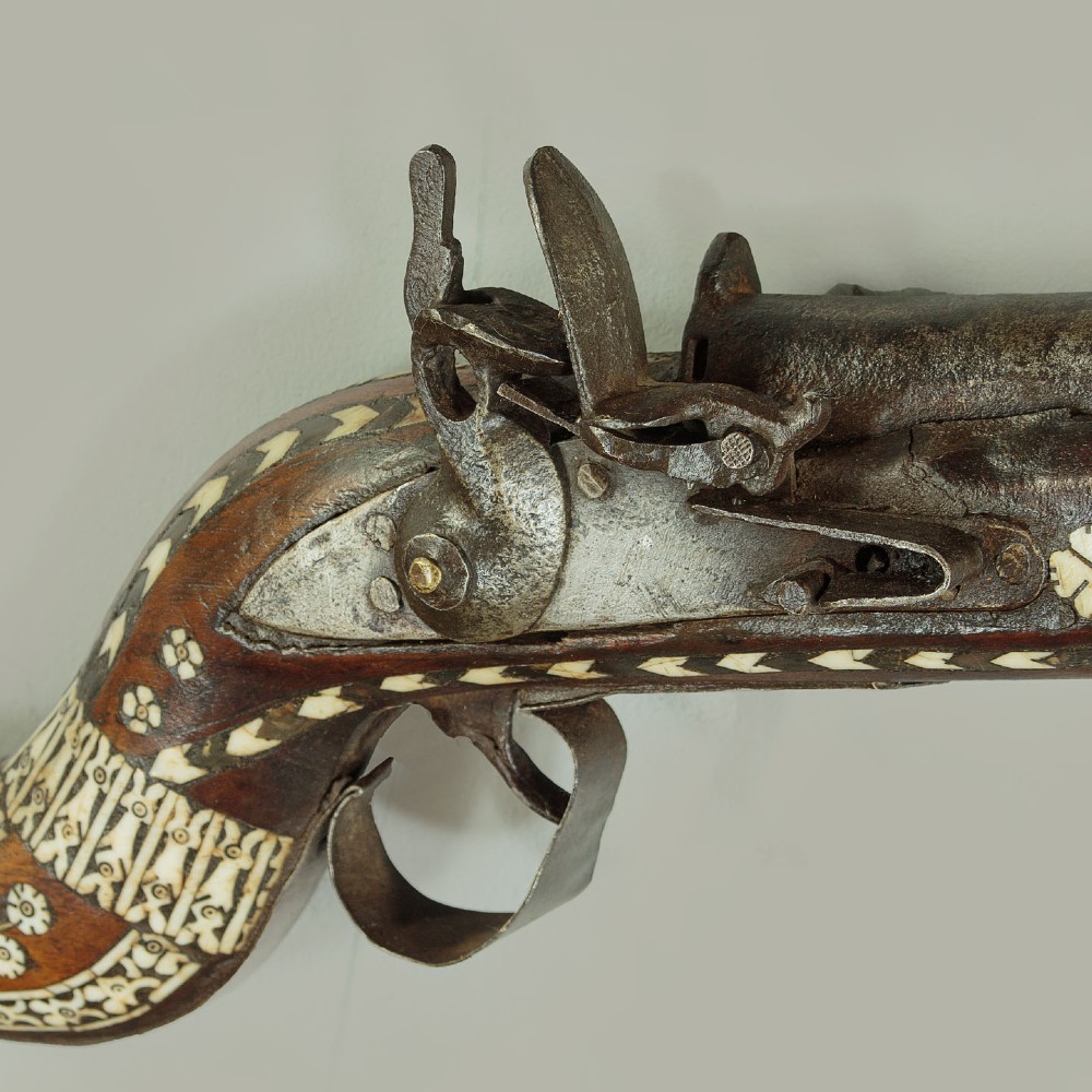 An antique Afghan Jezail musket featuring a distinctly curved wooden stock decorated with geometric bone inlay and a steel lock mechanism. View IV