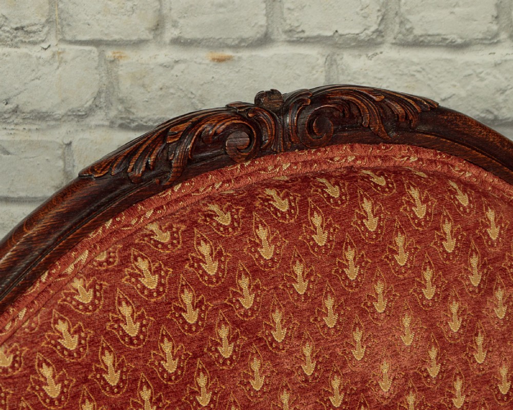 A c.1920 French-style upholstered day bed featuring a dark carved wooden frame, terracotta red patterned fabric, and matching tassel-trimmed cushions. View VI