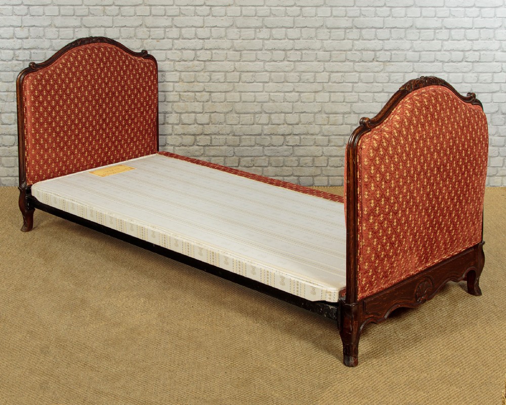 A c.1920 French-style upholstered day bed featuring a dark carved wooden frame, terracotta red patterned fabric, and matching tassel-trimmed cushions. View IX