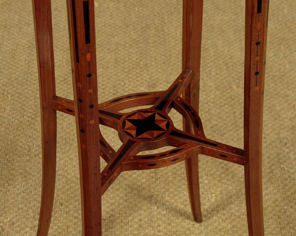 A tall, slender Edwardian specimen wood plant stand featuring geometric marquetry inlay on the top, apron, and legs, supported by four gently sweeping legs joined by an inlaid cross-stretcher. View VI