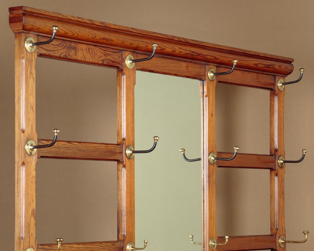 A large Victorian pine hallstand featuring a central vertical mirror, multiple brass coat hooks, inset ceramic tiles, a marble-topped glove drawer, and lower umbrella stand trays. View III