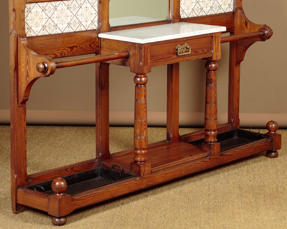 A large Victorian pine hallstand featuring a central vertical mirror, multiple brass coat hooks, inset ceramic tiles, a marble-topped glove drawer, and lower umbrella stand trays. View XI