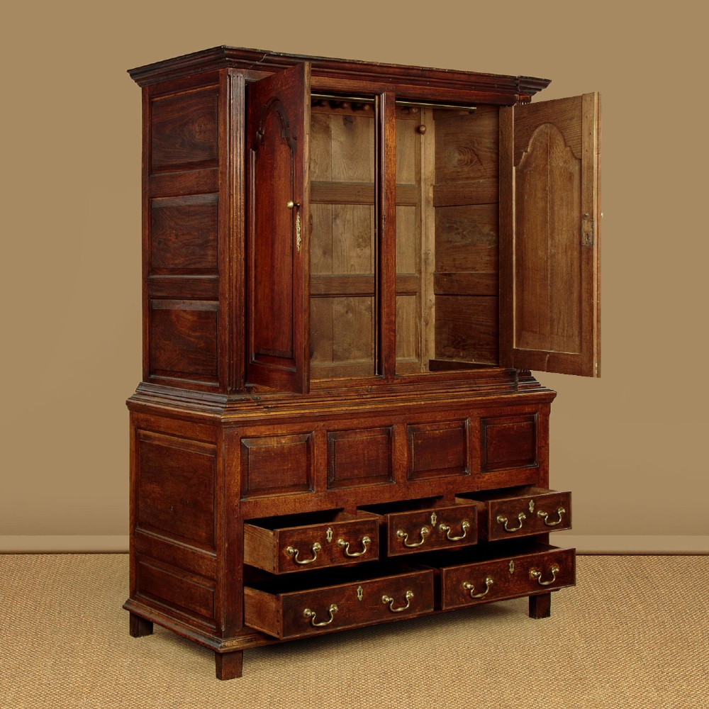 A tall 18th-century dark oak Georgian tack cupboard featuring twin arched panel doors over a base with five drawers and brass handles. View V