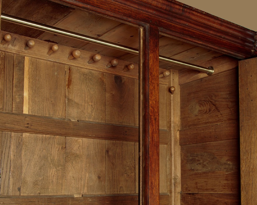 A tall 18th-century dark oak Georgian tack cupboard featuring twin arched panel doors over a base with five drawers and brass handles. View VIII