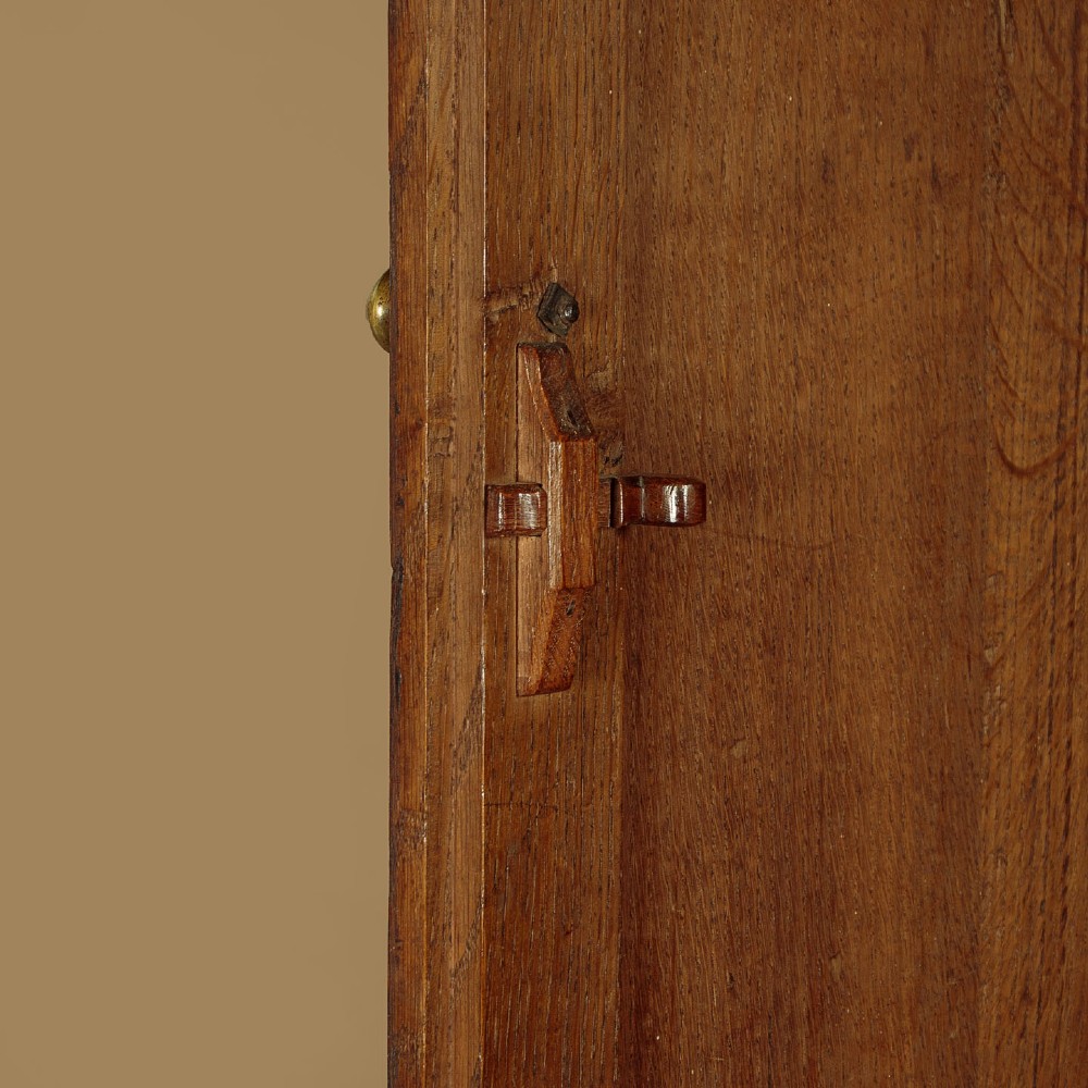 A tall 18th-century dark oak Georgian tack cupboard featuring twin arched panel doors over a base with five drawers and brass handles. View X