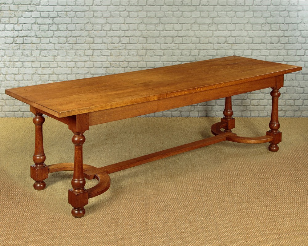 A long solid oak refectory dining table featuring turned legs and a low curved stretcher base.