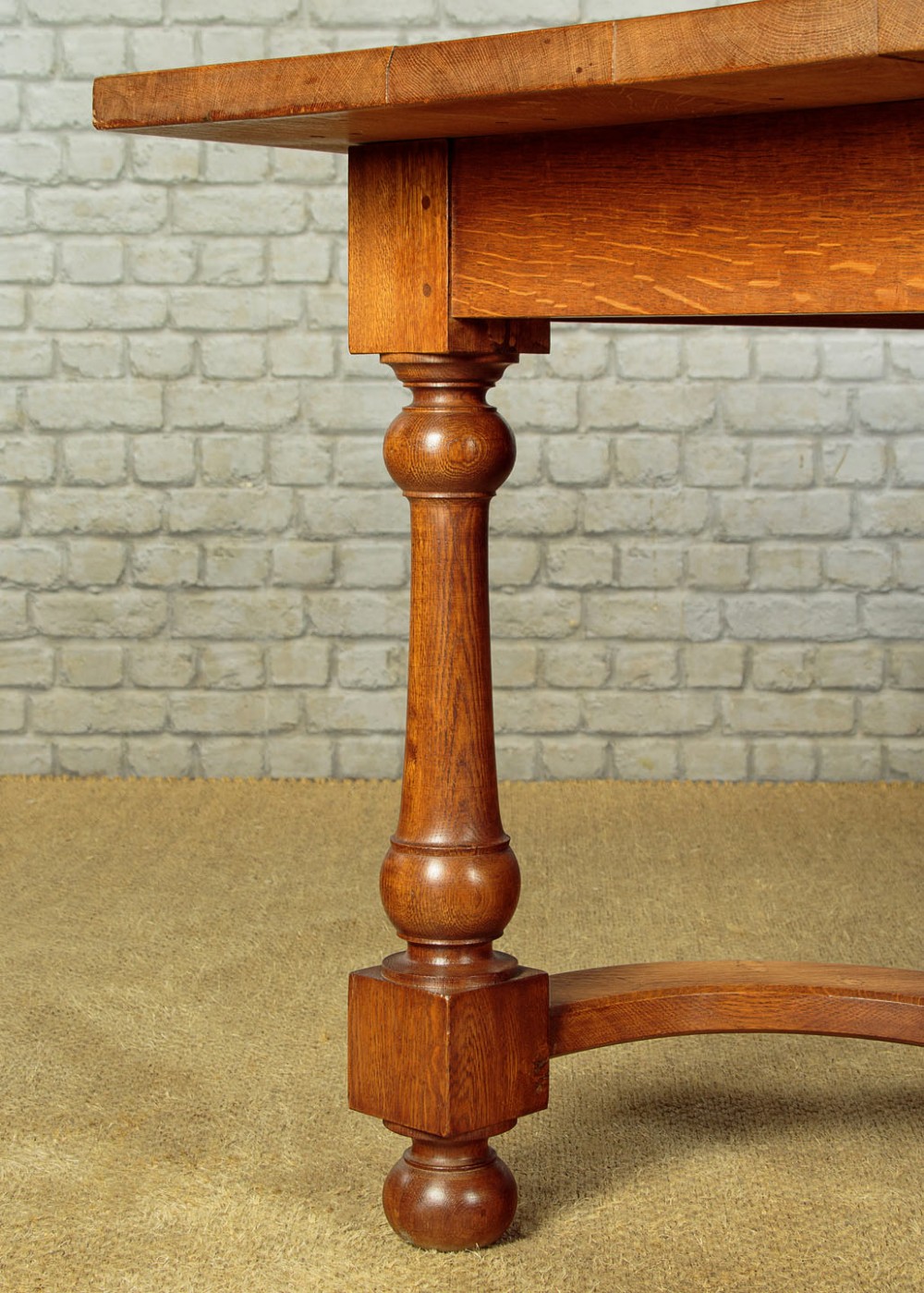 A long solid oak refectory dining table featuring turned legs and a low curved stretcher base. View IX