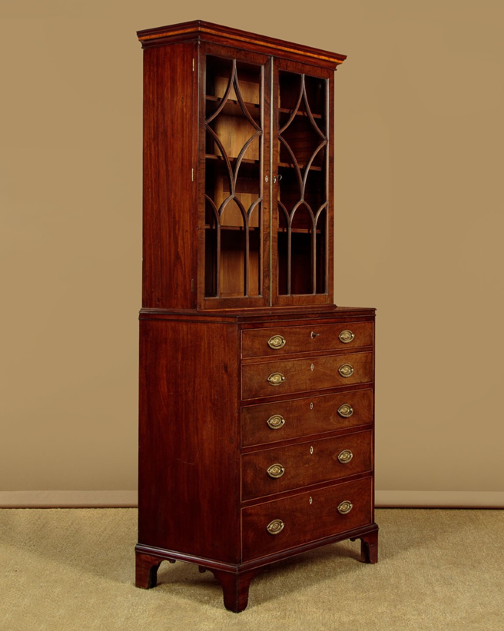 A tall mahogany secretaire bureau bookcase featuring two upper glazed doors with geometric astragal glazing over a chest of drawers with brass oval handles. View III