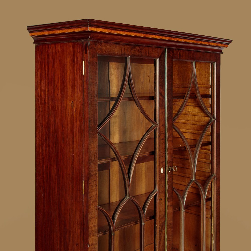 A tall mahogany secretaire bureau bookcase featuring two upper glazed doors with geometric astragal glazing over a chest of drawers with brass oval handles. View VI