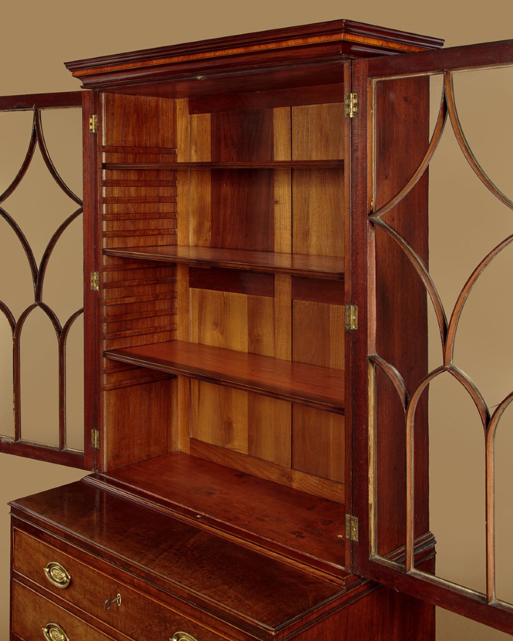 A tall mahogany secretaire bureau bookcase featuring two upper glazed doors with geometric astragal glazing over a chest of drawers with brass oval handles. View VII