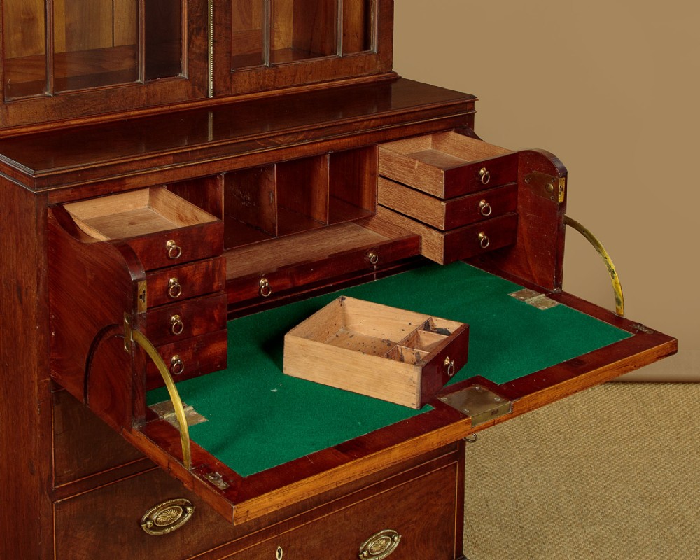 A tall mahogany secretaire bureau bookcase featuring two upper glazed doors with geometric astragal glazing over a chest of drawers with brass oval handles. View IX