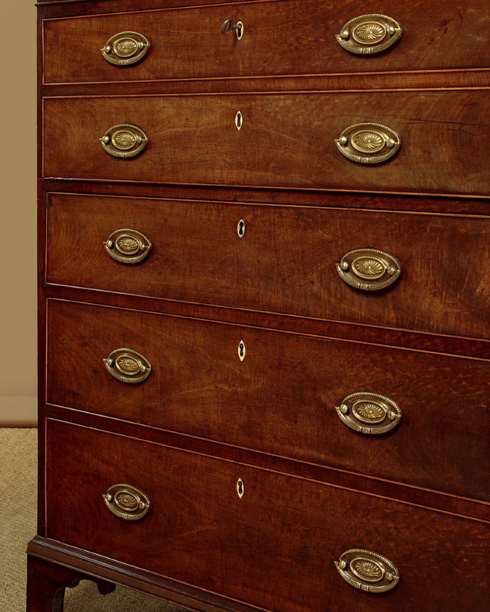 A tall mahogany secretaire bureau bookcase featuring two upper glazed doors with geometric astragal glazing over a chest of drawers with brass oval handles. View X