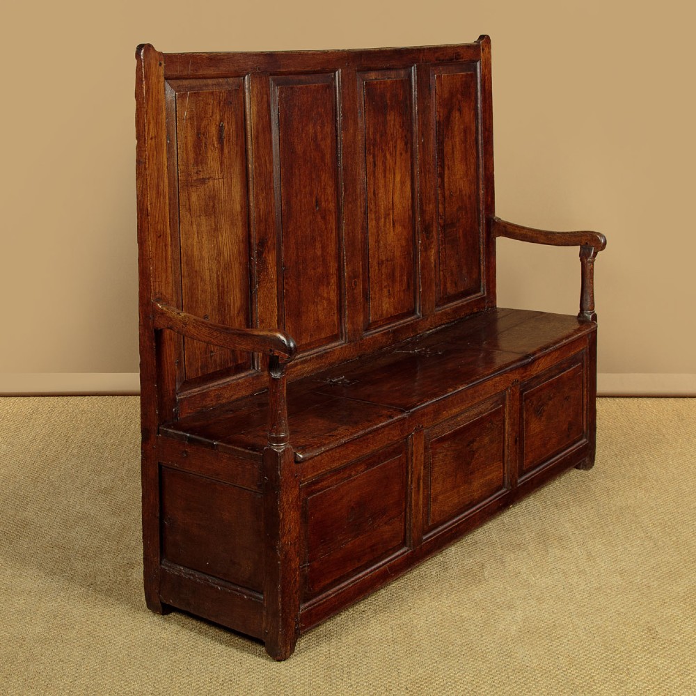 A dark oak 18th-century high-back box settle featuring fielded panels, shaped open armrests, and a hinged lid seat. View II