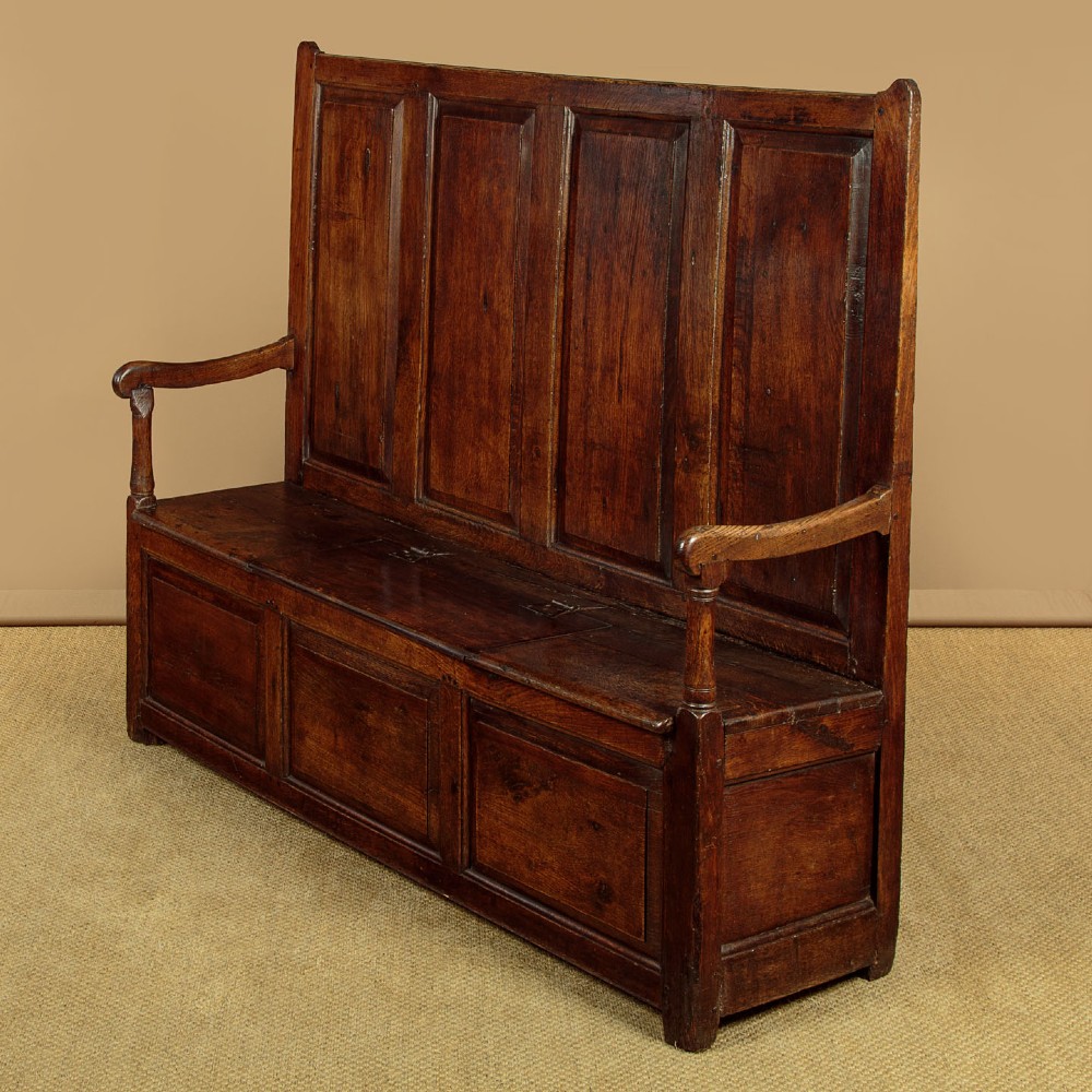 A dark oak 18th-century high-back box settle featuring fielded panels, shaped open armrests, and a hinged lid seat. View III