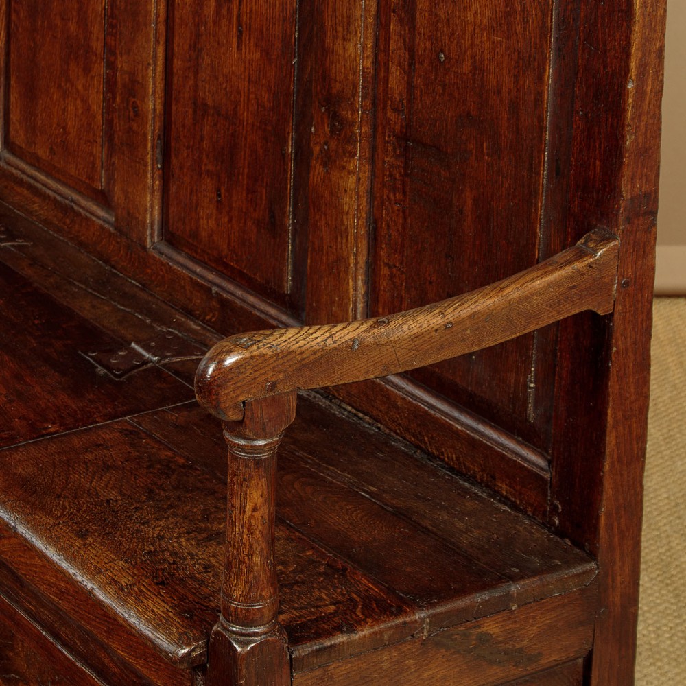 A dark oak 18th-century high-back box settle featuring fielded panels, shaped open armrests, and a hinged lid seat. View VIII