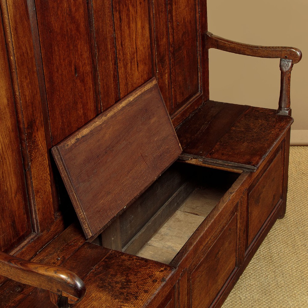 A dark oak 18th-century high-back box settle featuring fielded panels, shaped open armrests, and a hinged lid seat. View XI