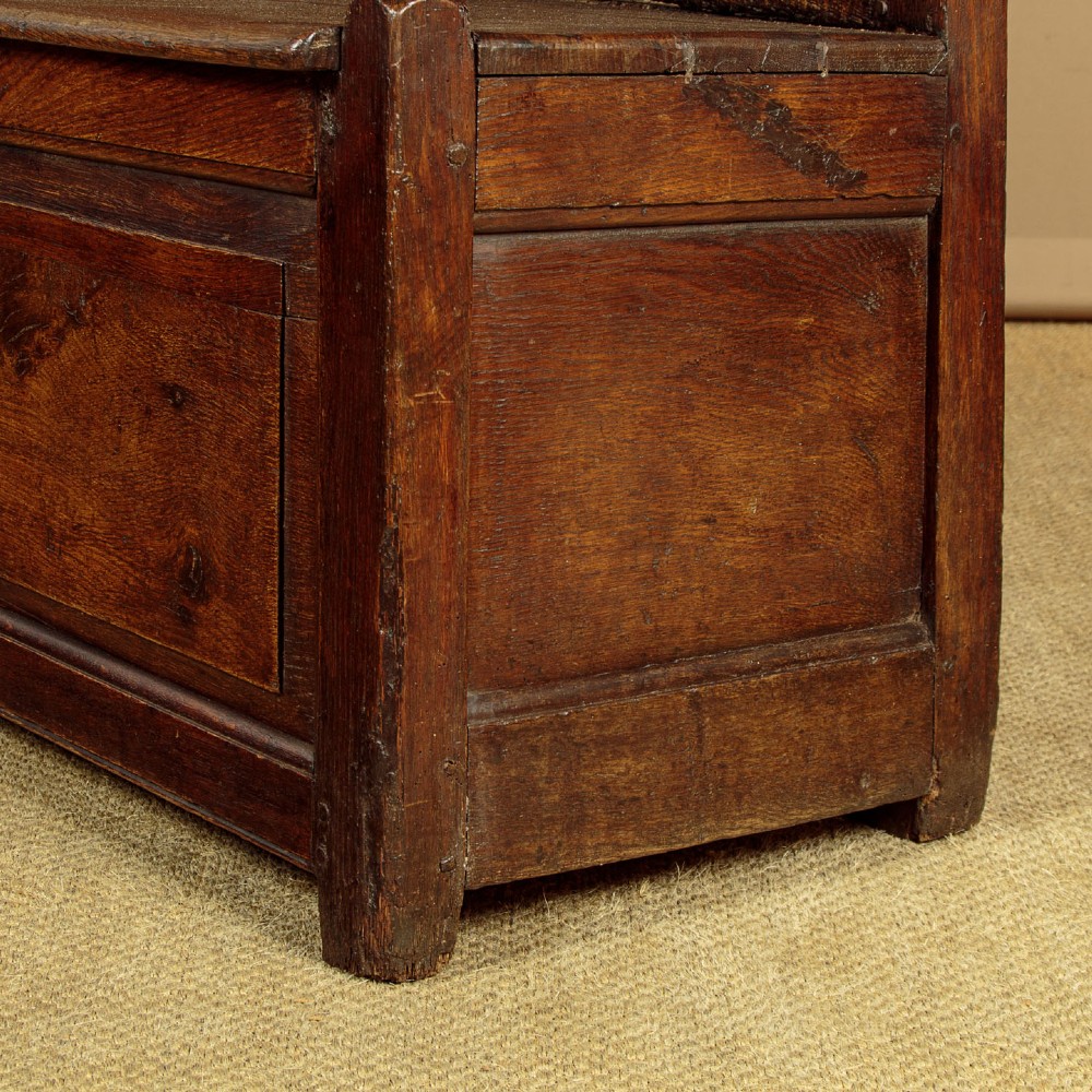 A dark oak 18th-century high-back box settle featuring fielded panels, shaped open armrests, and a hinged lid seat. View XII