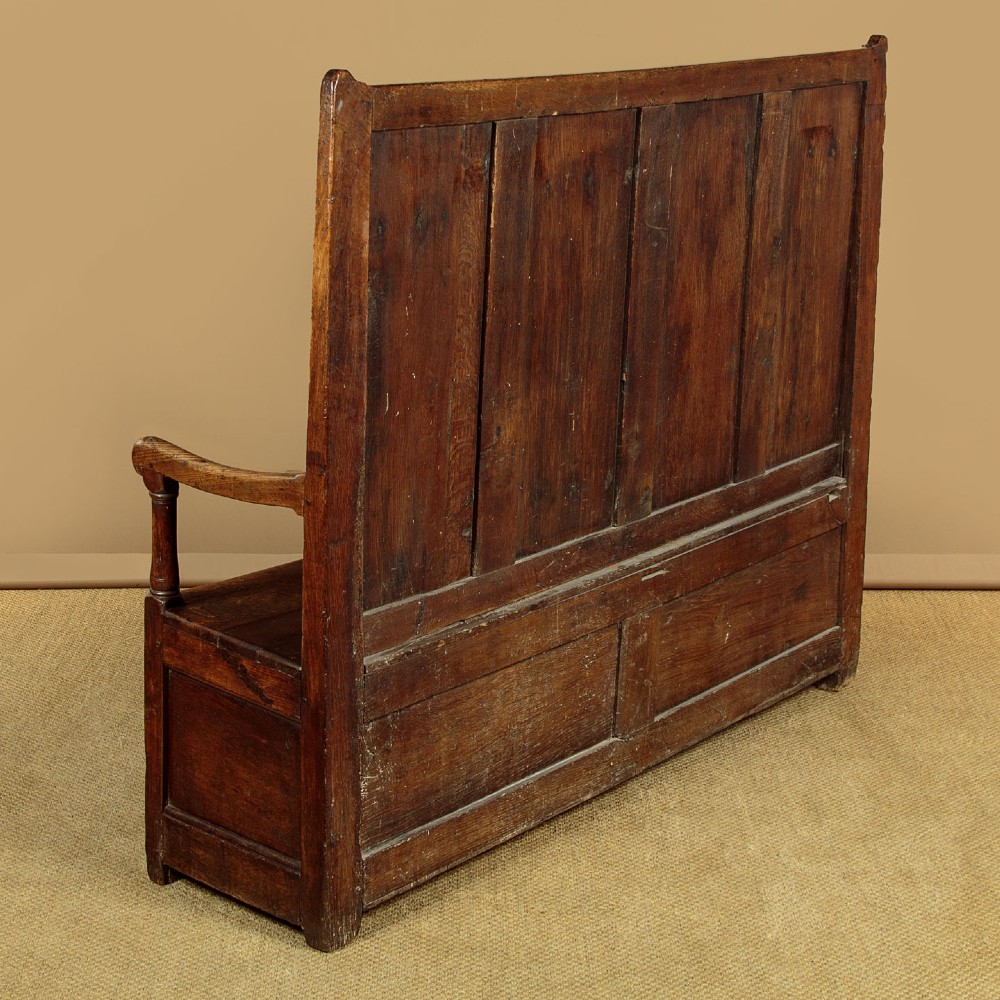 A dark oak 18th-century high-back box settle featuring fielded panels, shaped open armrests, and a hinged lid seat. View XIII