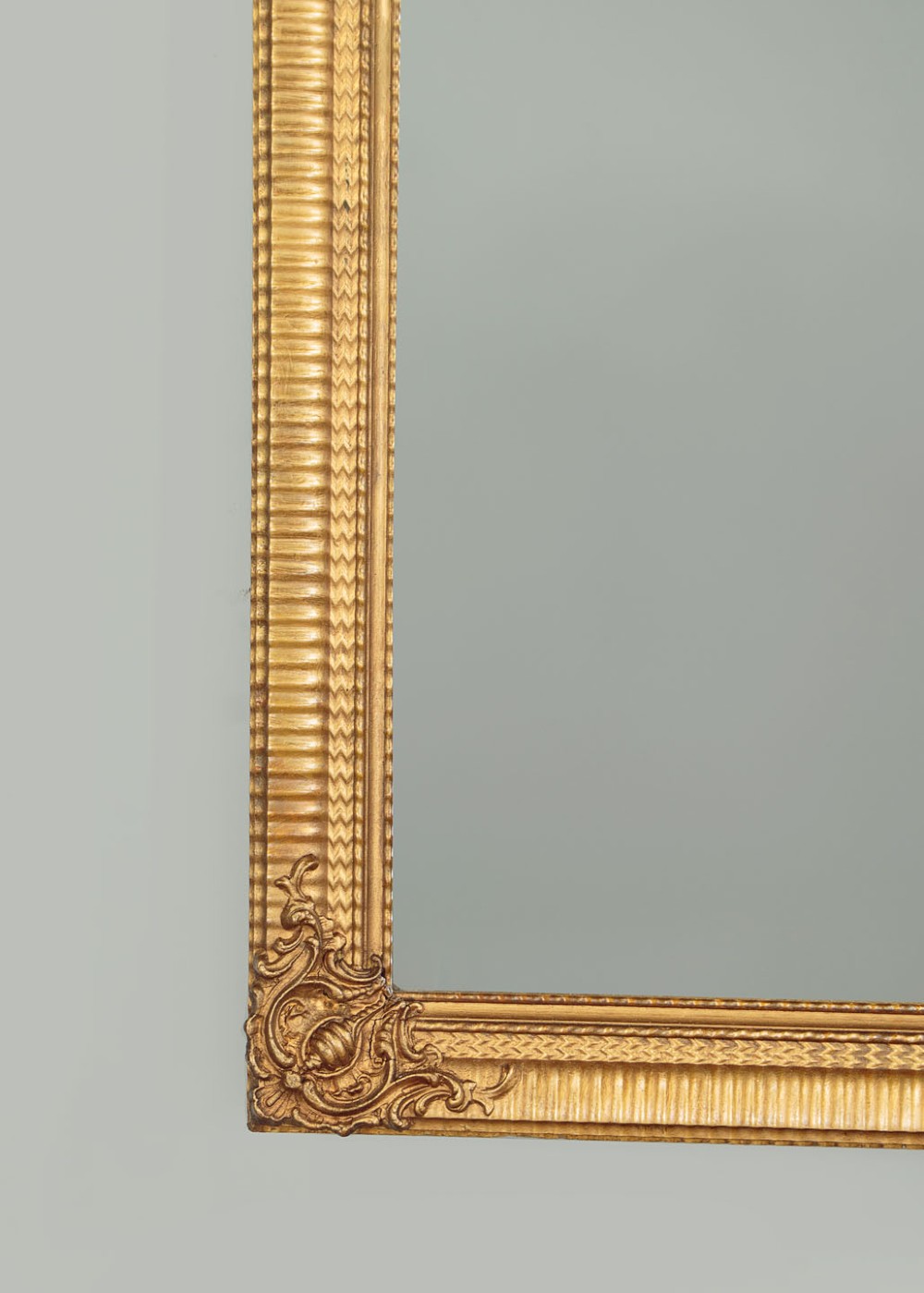 A rectangular wall mirror featuring a gilded frame with reeded moulding and carved scrollwork details in each corner. View VI