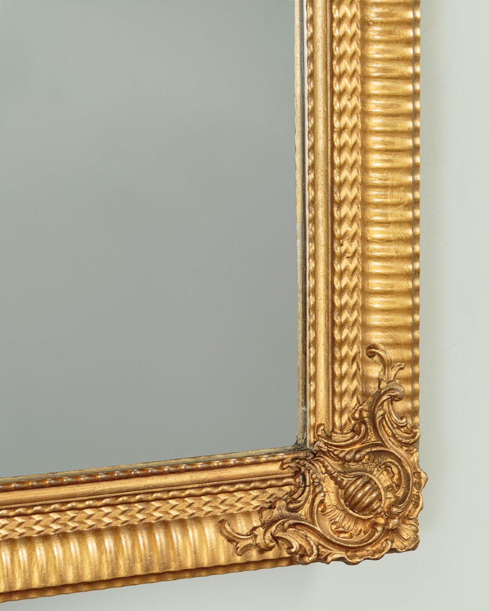 A rectangular wall mirror featuring a gilded frame with reeded moulding and carved scrollwork details in each corner. View VII