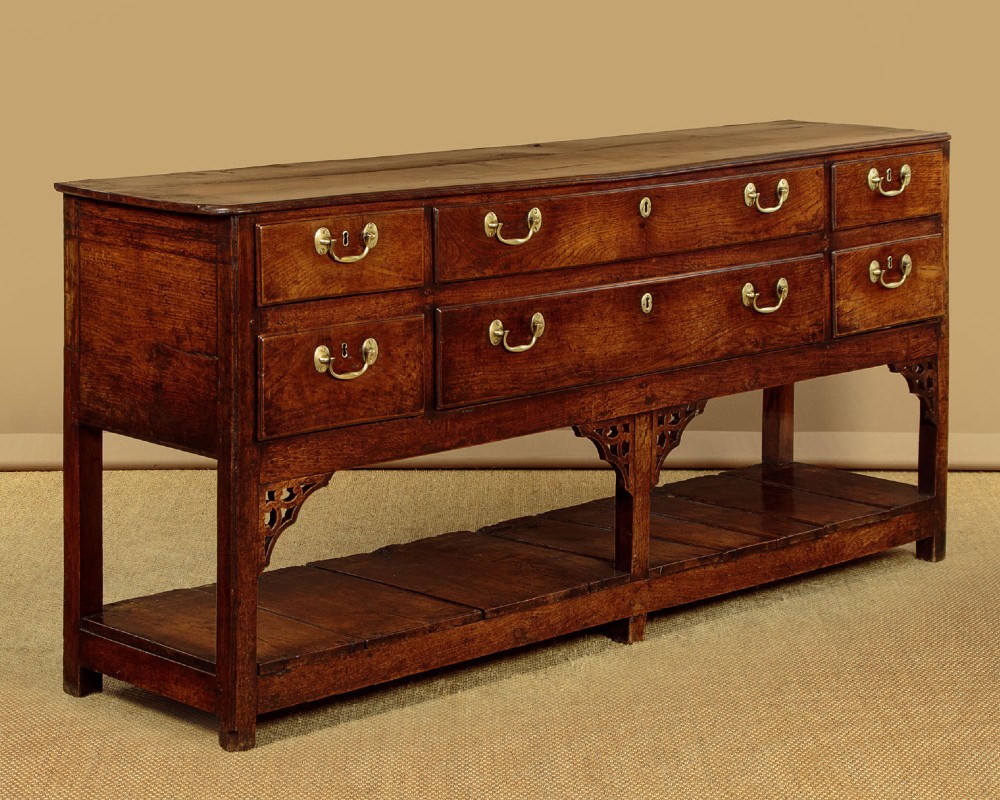 A eighteenth-century Georgian dark oak potboard dresser base featuring six drawer fronts with brass swan-neck handles and an open lower shelf.