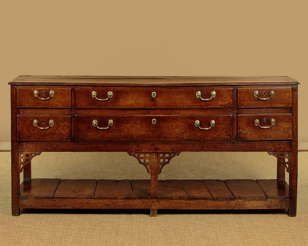 A eighteenth-century Georgian dark oak potboard dresser base featuring six drawer fronts with brass swan-neck handles and an open lower shelf. View V