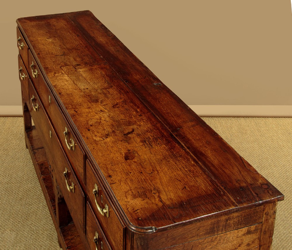 A eighteenth-century Georgian dark oak potboard dresser base featuring six drawer fronts with brass swan-neck handles and an open lower shelf. View VI