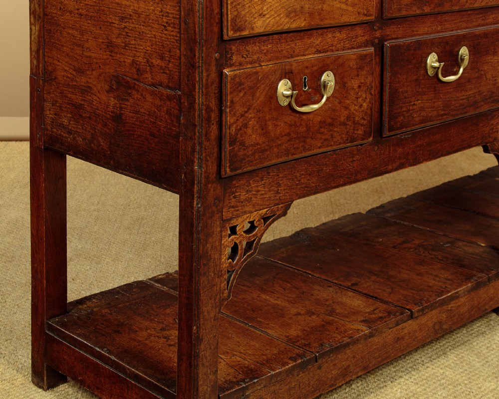 A eighteenth-century Georgian dark oak potboard dresser base featuring six drawer fronts with brass swan-neck handles and an open lower shelf. View XII