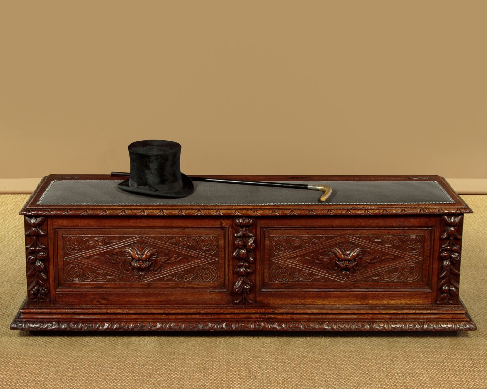 A long late Victorian dark oak ottoman box seat featuring an inset leather top with brass studding, carved relief mask panels, and a heavy moulded base. View II