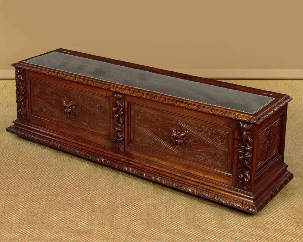 A long late Victorian dark oak ottoman box seat featuring an inset leather top with brass studding, carved relief mask panels, and a heavy moulded base. View III