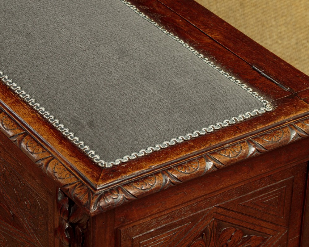 A long late Victorian dark oak ottoman box seat featuring an inset leather top with brass studding, carved relief mask panels, and a heavy moulded base. View V