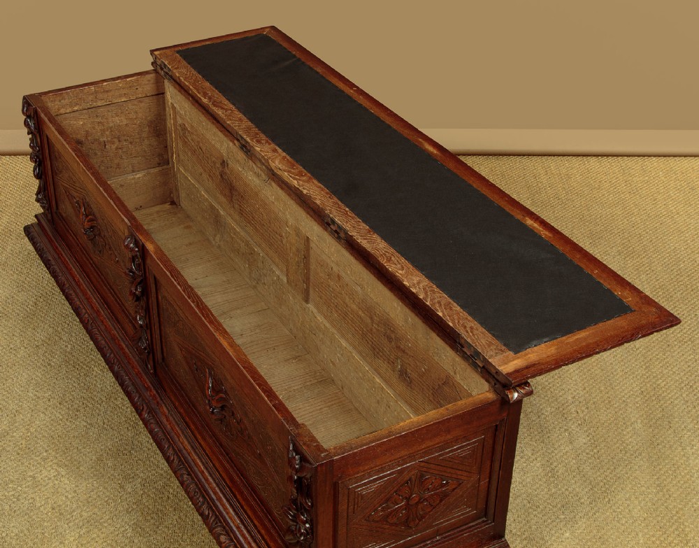 A long late Victorian dark oak ottoman box seat featuring an inset leather top with brass studding, carved relief mask panels, and a heavy moulded base. View VI