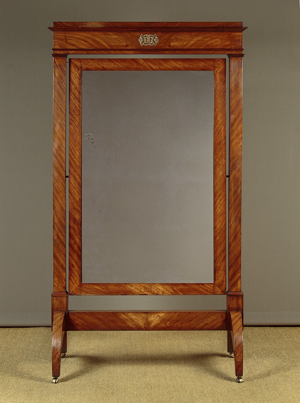 A mid-19th-century mahogany cheval mirror featuring a rectangular swivelling frame set between upright supports with an architectural corniced top and brass mount, resting on splayed feet with castors.