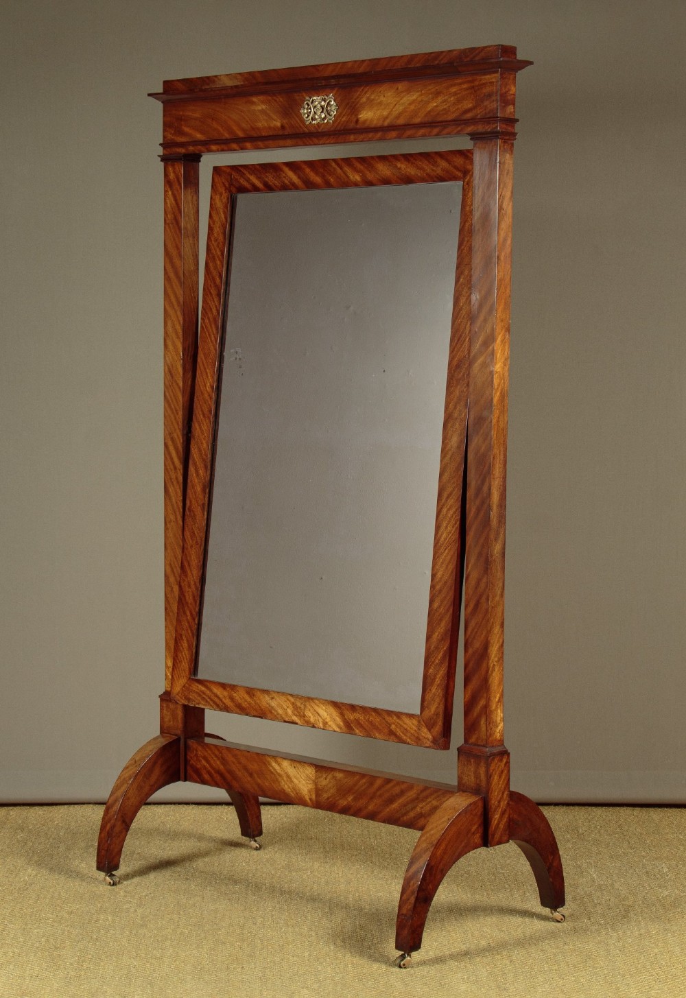 A mid-19th-century mahogany cheval mirror featuring a rectangular swivelling frame set between upright supports with an architectural corniced top and brass mount, resting on splayed feet with castors. View II