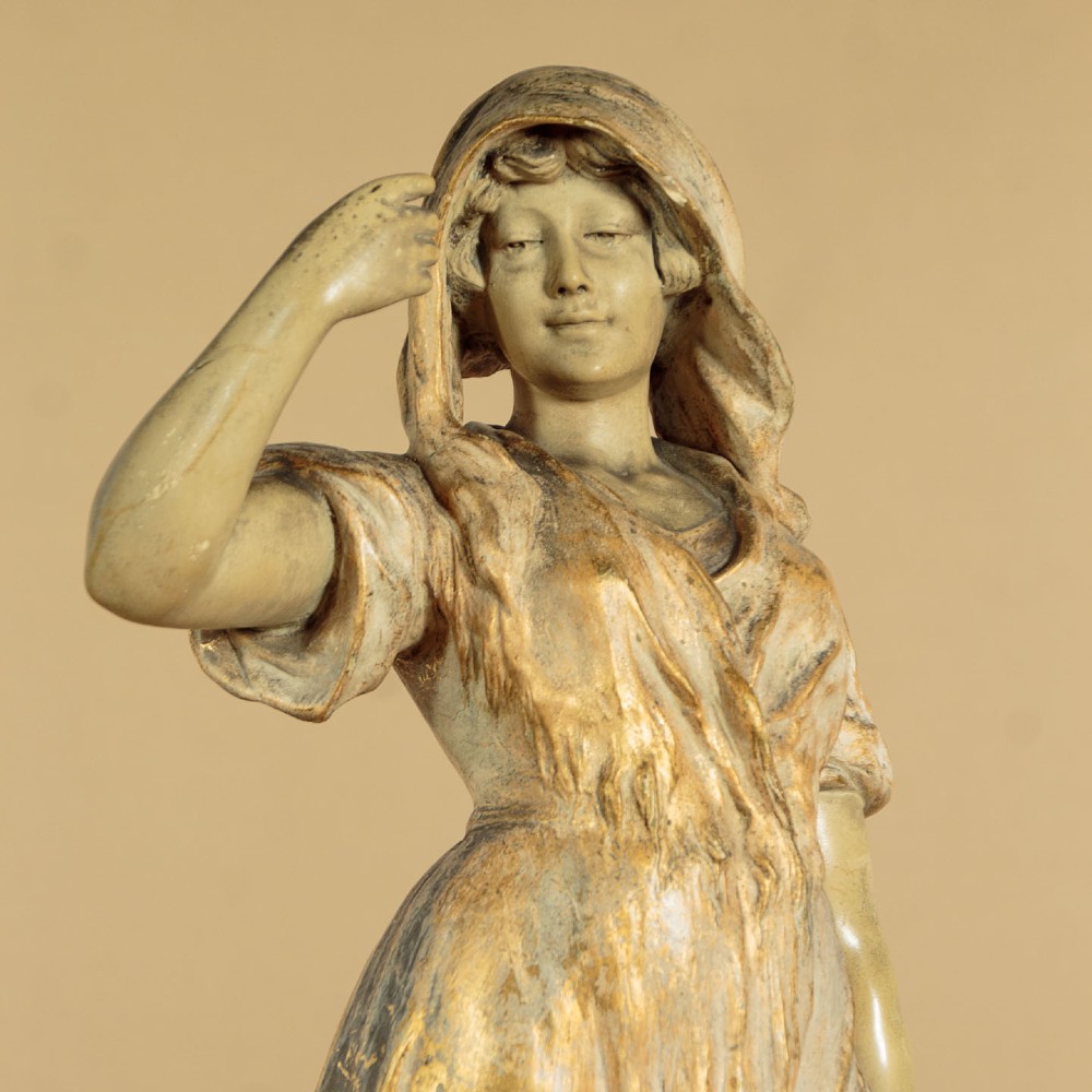 A turn-of-the-century terracotta sculpture depicting a standing young woman in rural dress wearing a headscarf and clogs, holding a basket. View III