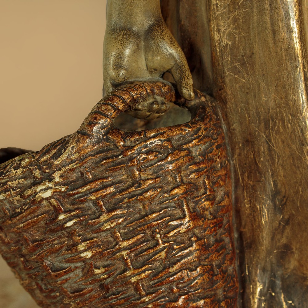 A turn-of-the-century terracotta sculpture depicting a standing young woman in rural dress wearing a headscarf and clogs, holding a basket. View IX