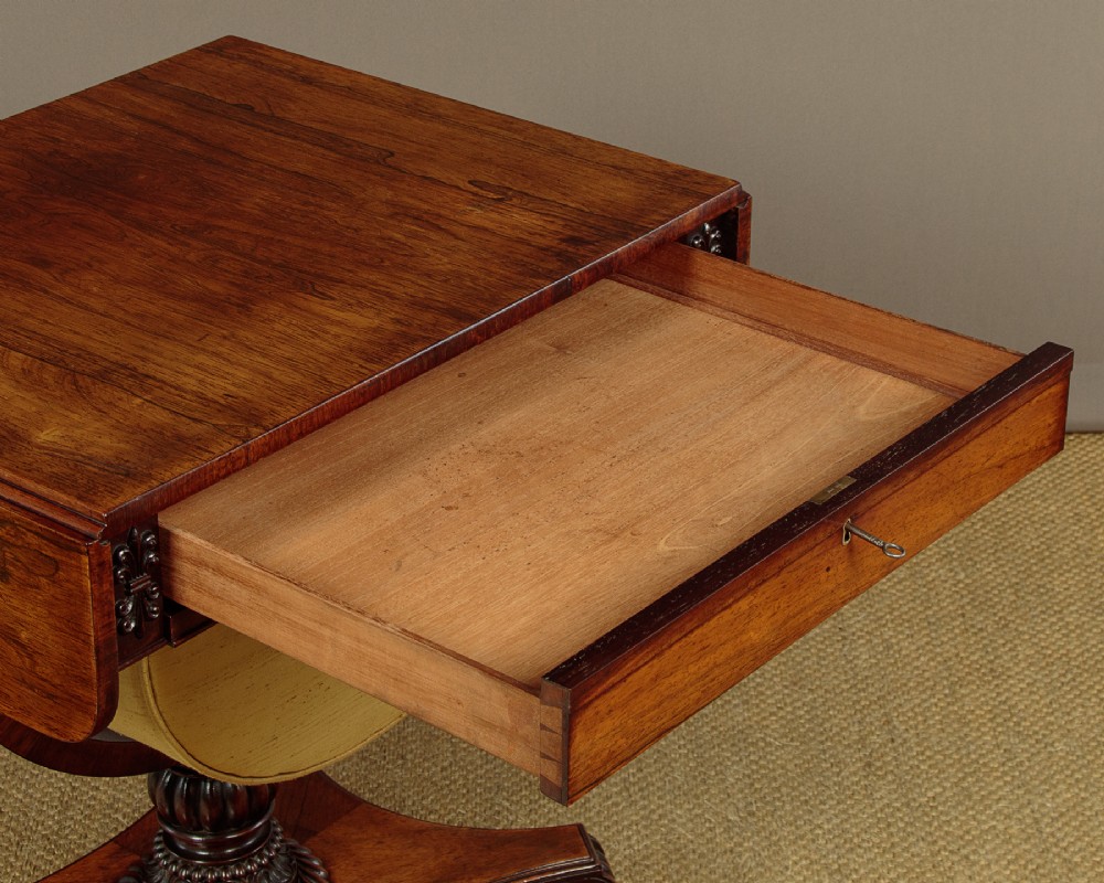 A nineteenth-century rosewood Pembroke side table with drop-leaf sides, a fabric work basket, turned column, and carved scroll feet. View V