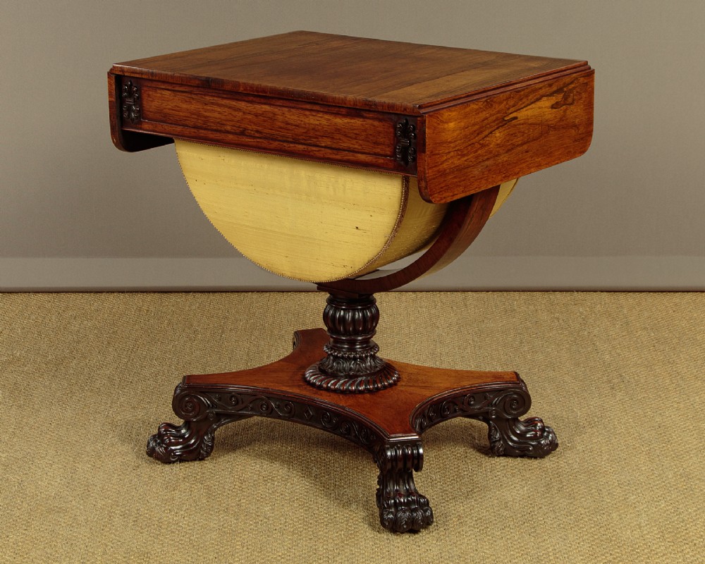 A nineteenth-century rosewood Pembroke side table with drop-leaf sides, a fabric work basket, turned column, and carved scroll feet. View X