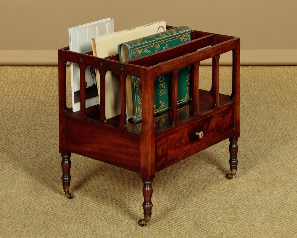 A dark mahogany Canterbury featuring four open slatted dividers above a single drawer with turned legs and brass castors. View II