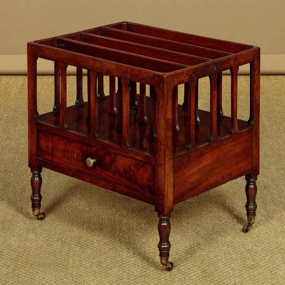 A dark mahogany Canterbury featuring four open slatted dividers above a single drawer with turned legs and brass castors. View III