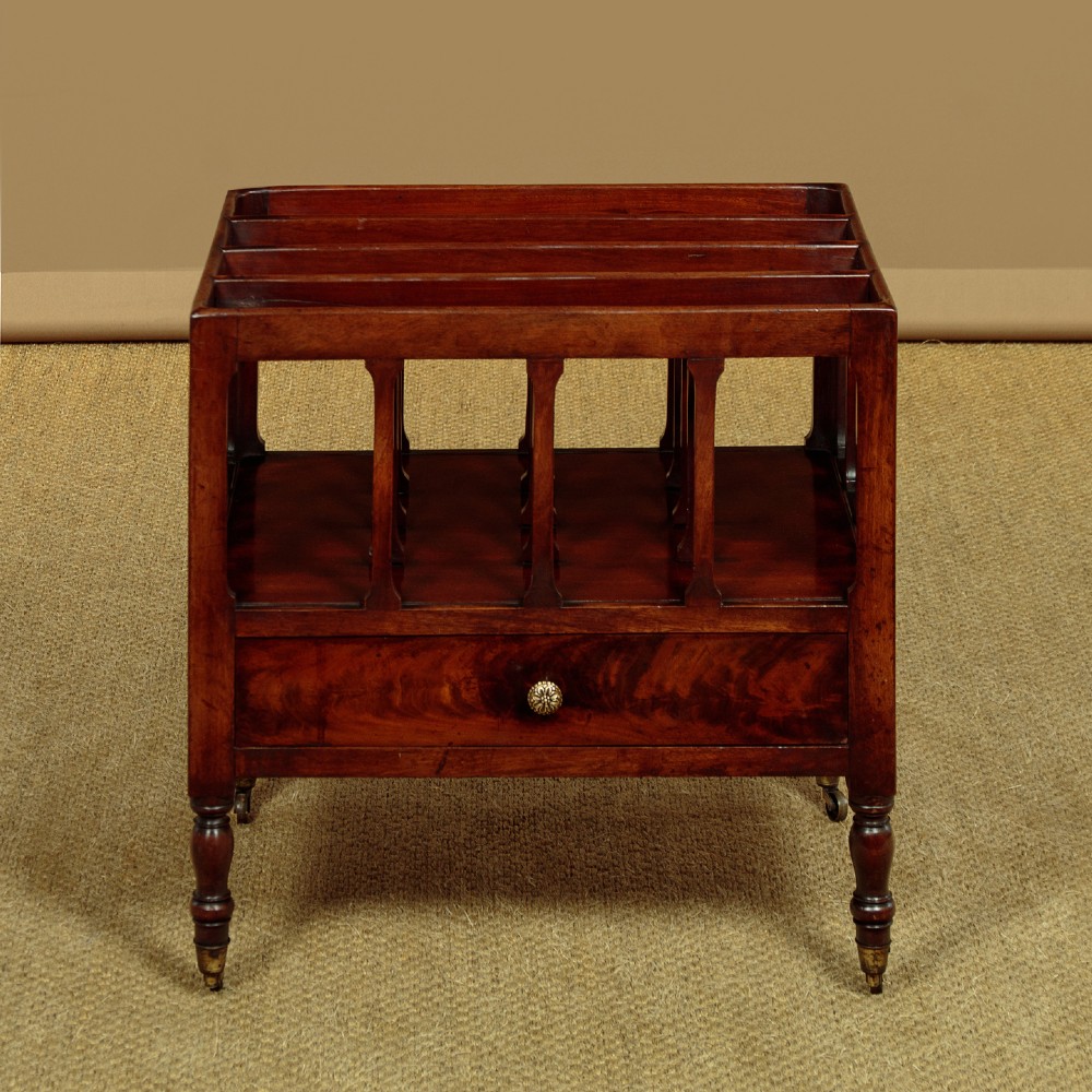 A dark mahogany Canterbury featuring four open slatted dividers above a single drawer with turned legs and brass castors. View IV