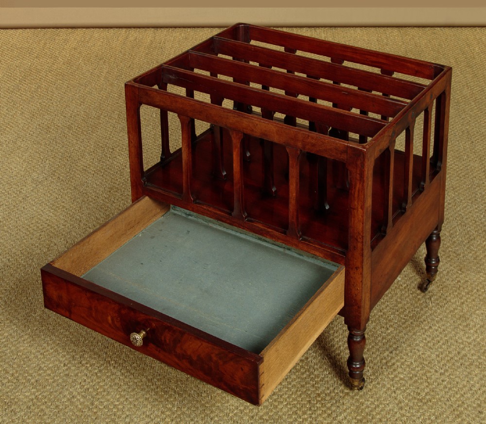 A dark mahogany Canterbury featuring four open slatted dividers above a single drawer with turned legs and brass castors. View VI