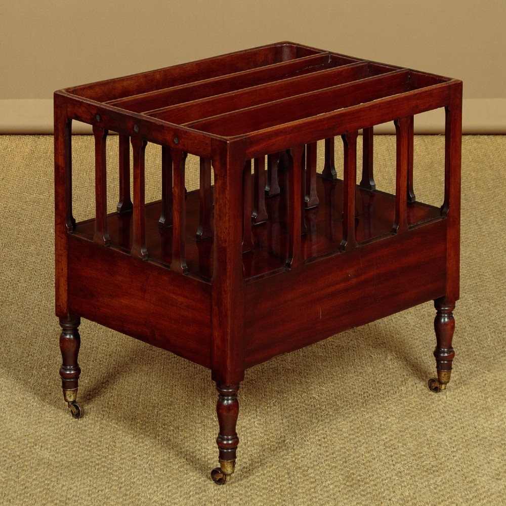 A dark mahogany Canterbury featuring four open slatted dividers above a single drawer with turned legs and brass castors. View IX