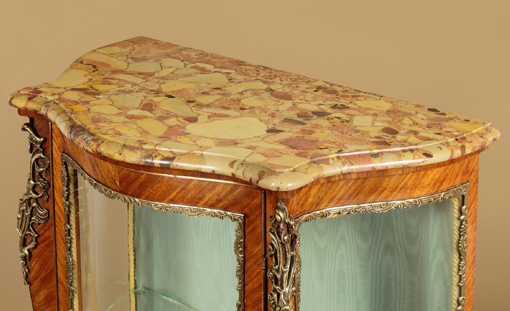 A small French Louis XV style vitrine with curved glass sides, a single glazed door, gilded brass mounts, a marble top, and a pale green fabric-lined interior with glass shelves. View V