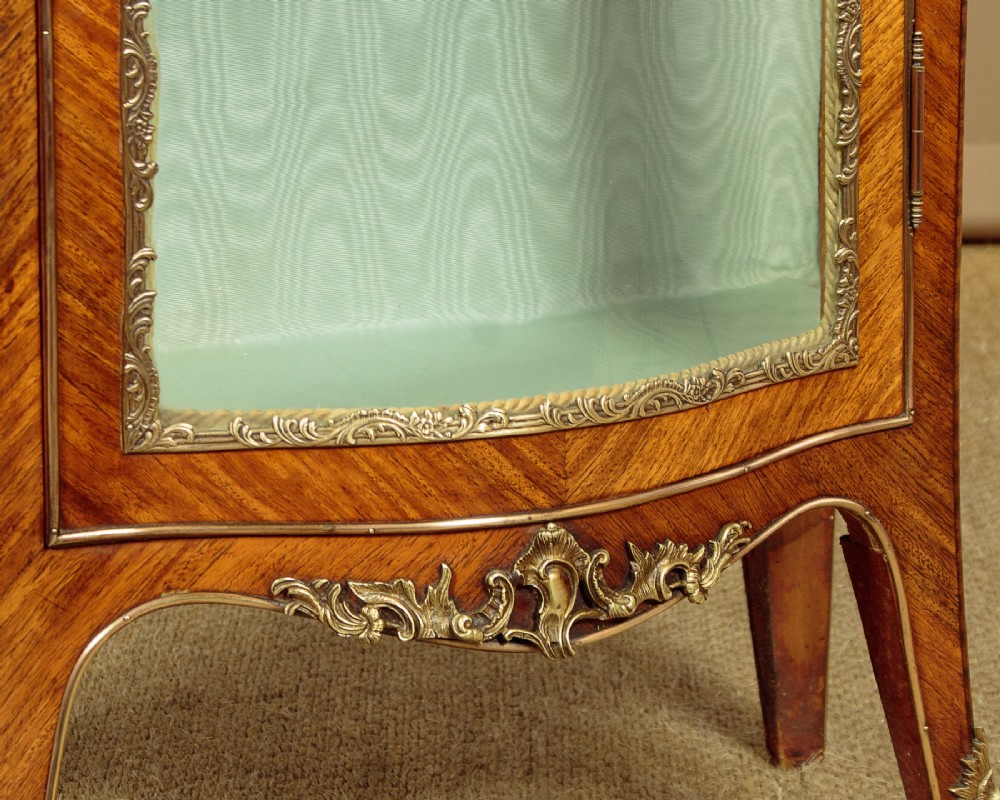 A small French Louis XV style vitrine with curved glass sides, a single glazed door, gilded brass mounts, a marble top, and a pale green fabric-lined interior with glass shelves. View XI