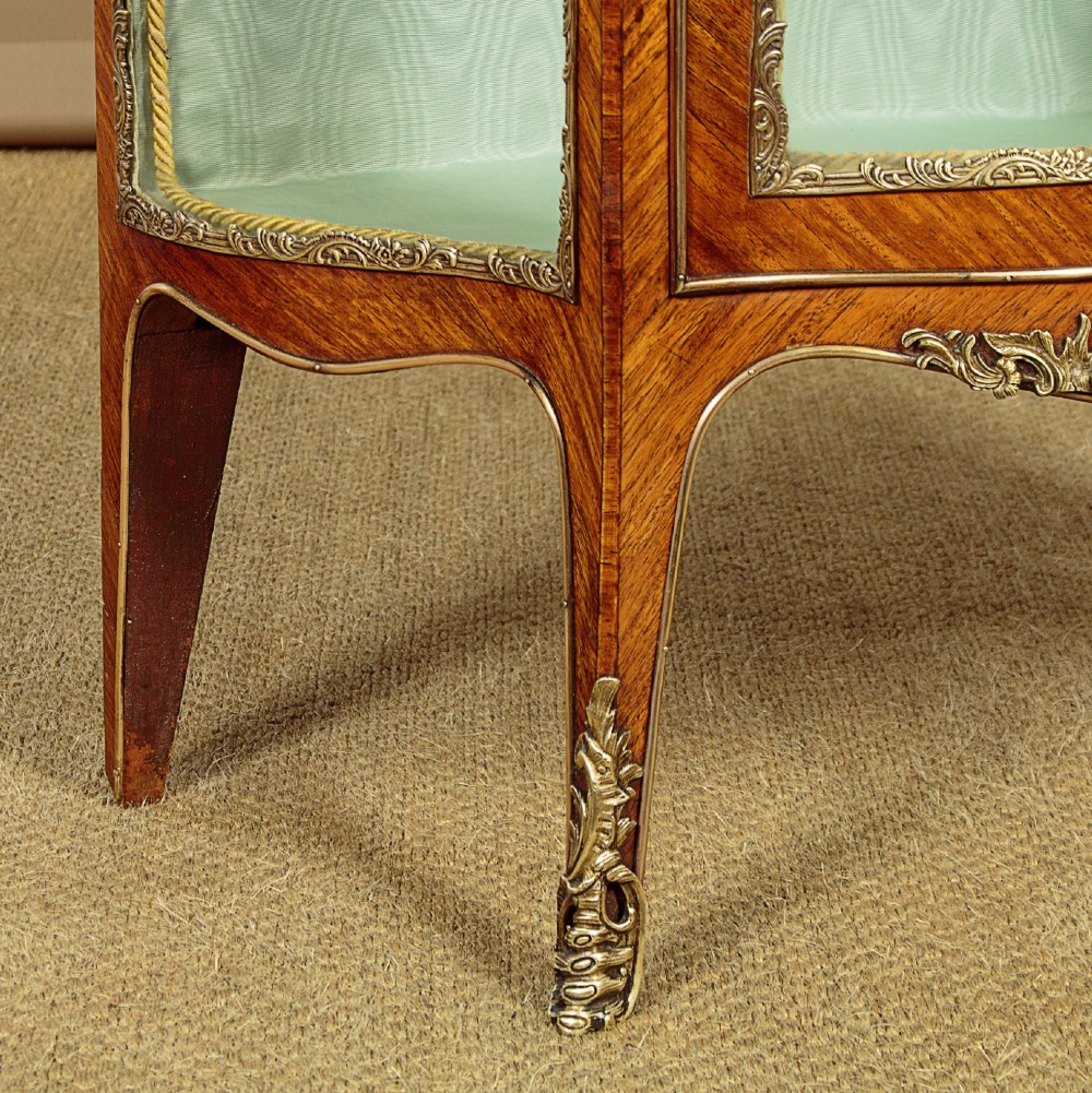 A small French Louis XV style vitrine with curved glass sides, a single glazed door, gilded brass mounts, a marble top, and a pale green fabric-lined interior with glass shelves. View XII
