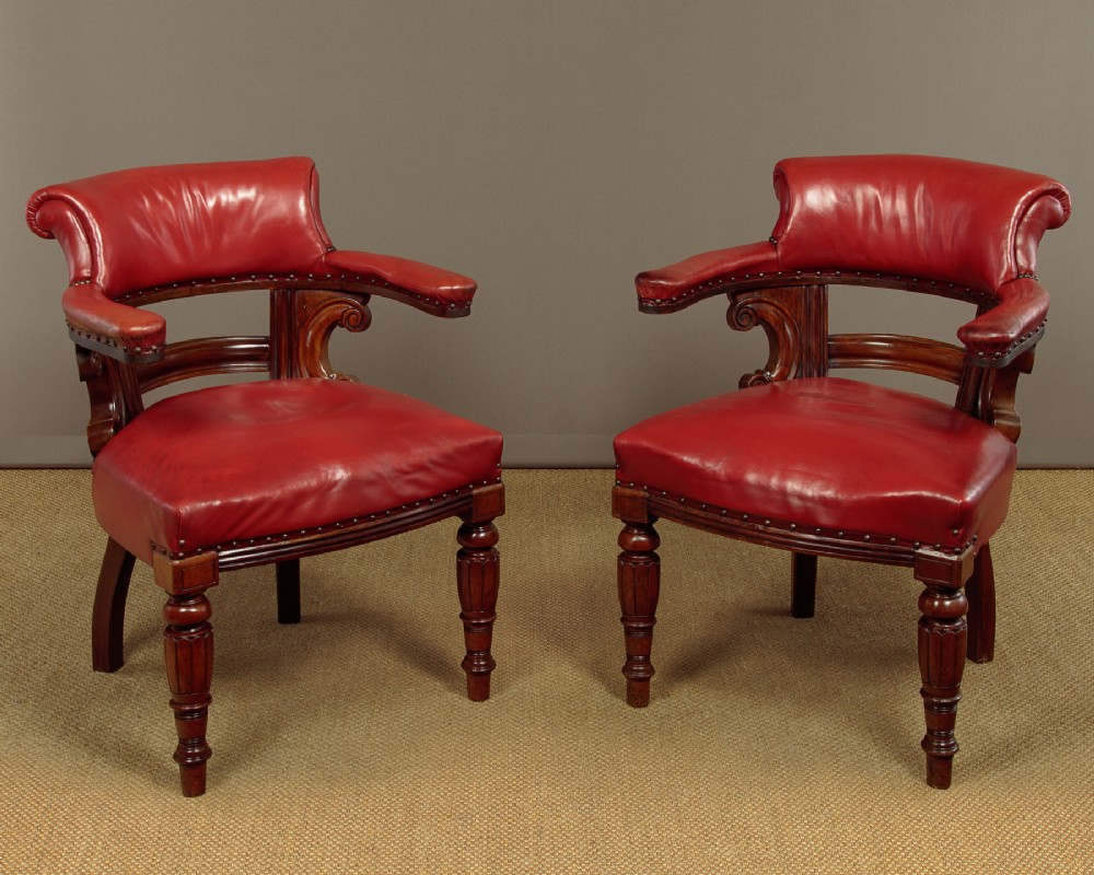 A pair of late Victorian walnut tub armchairs with red leather upholstery, studded brass trim, turned front legs, and carved scroll arm supports.