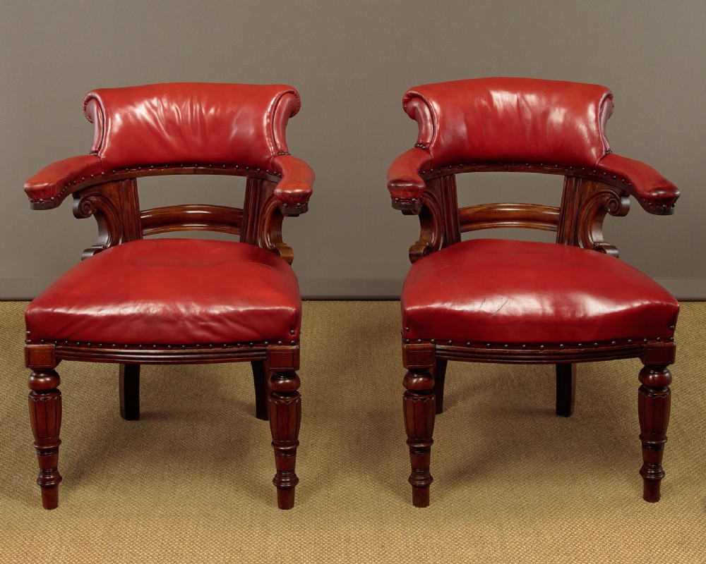 A pair of late Victorian walnut tub armchairs with red leather upholstery, studded brass trim, turned front legs, and carved scroll arm supports. View II