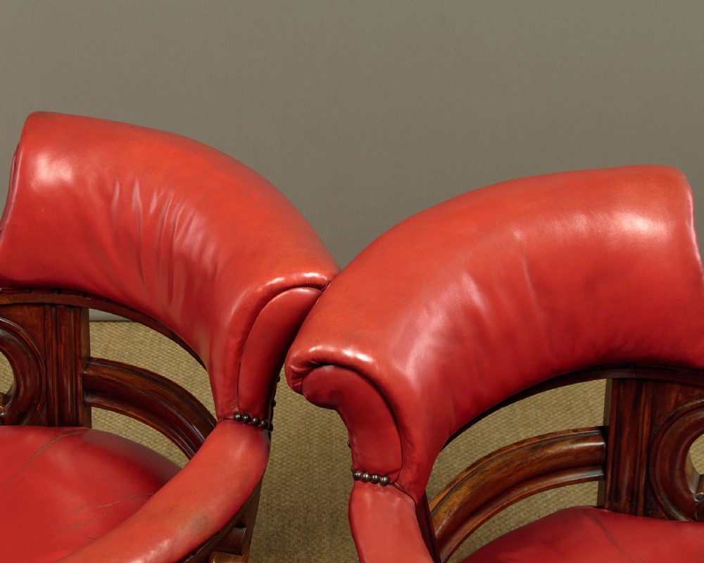 A pair of late Victorian walnut tub armchairs with red leather upholstery, studded brass trim, turned front legs, and carved scroll arm supports. View III